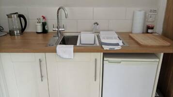 Een kleine keuken met een spoelbak, een koffiezetapparaat, een waterkoker en een afdruiprek.