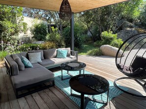 En udendørs patio med sofa, runde borde og en hængekøjsstol.