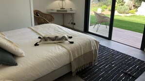 A bedroom with a large bed, a bedside table with a lamp, a chair, and a view of a garden through a sliding door. - New villa 185m2 located close to beaches, port and city center (Porto-Vecchio)