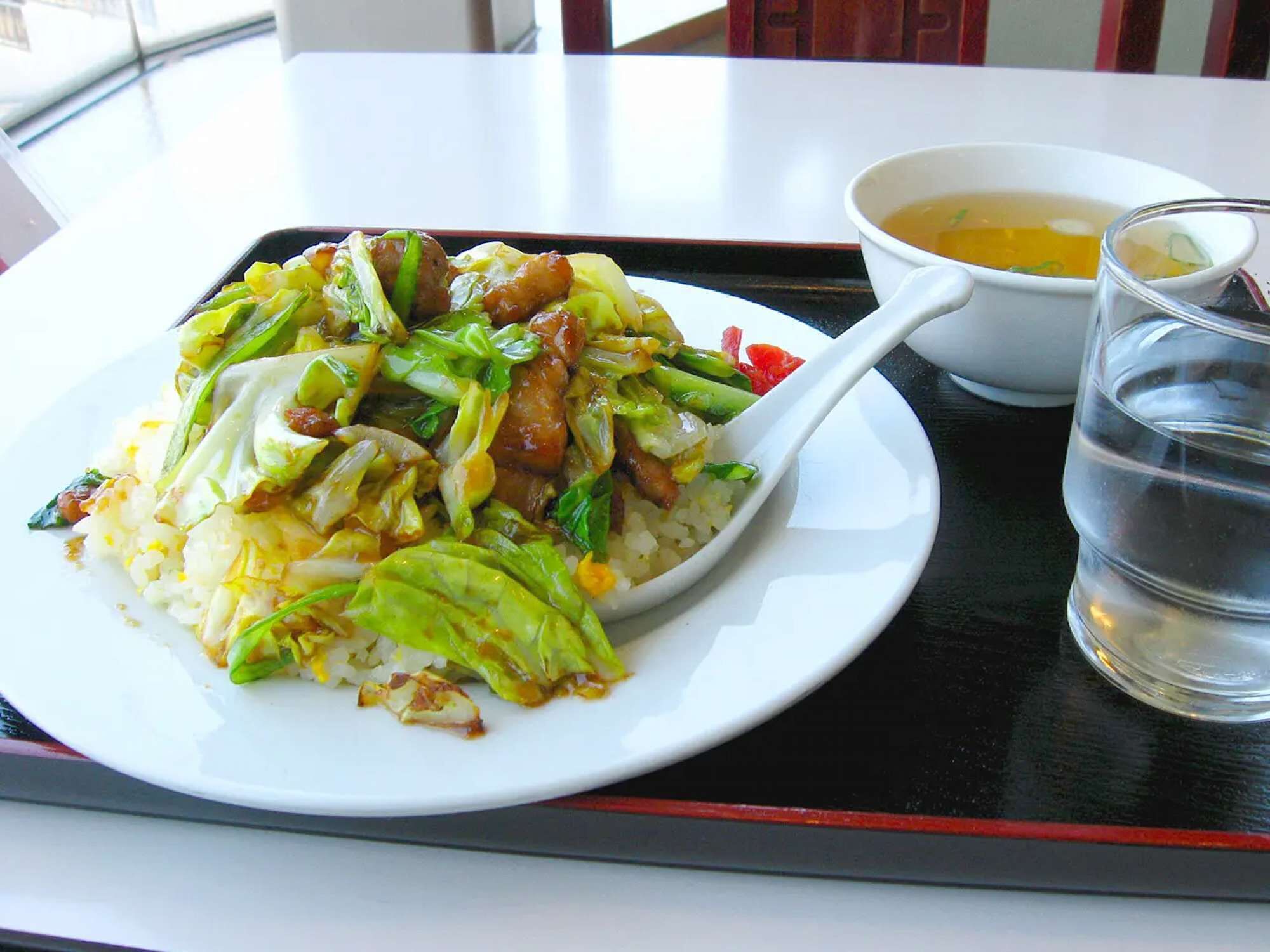 A plate of stir-fried vegetables and rice on a tray with a bowl of soup and a glass of water.