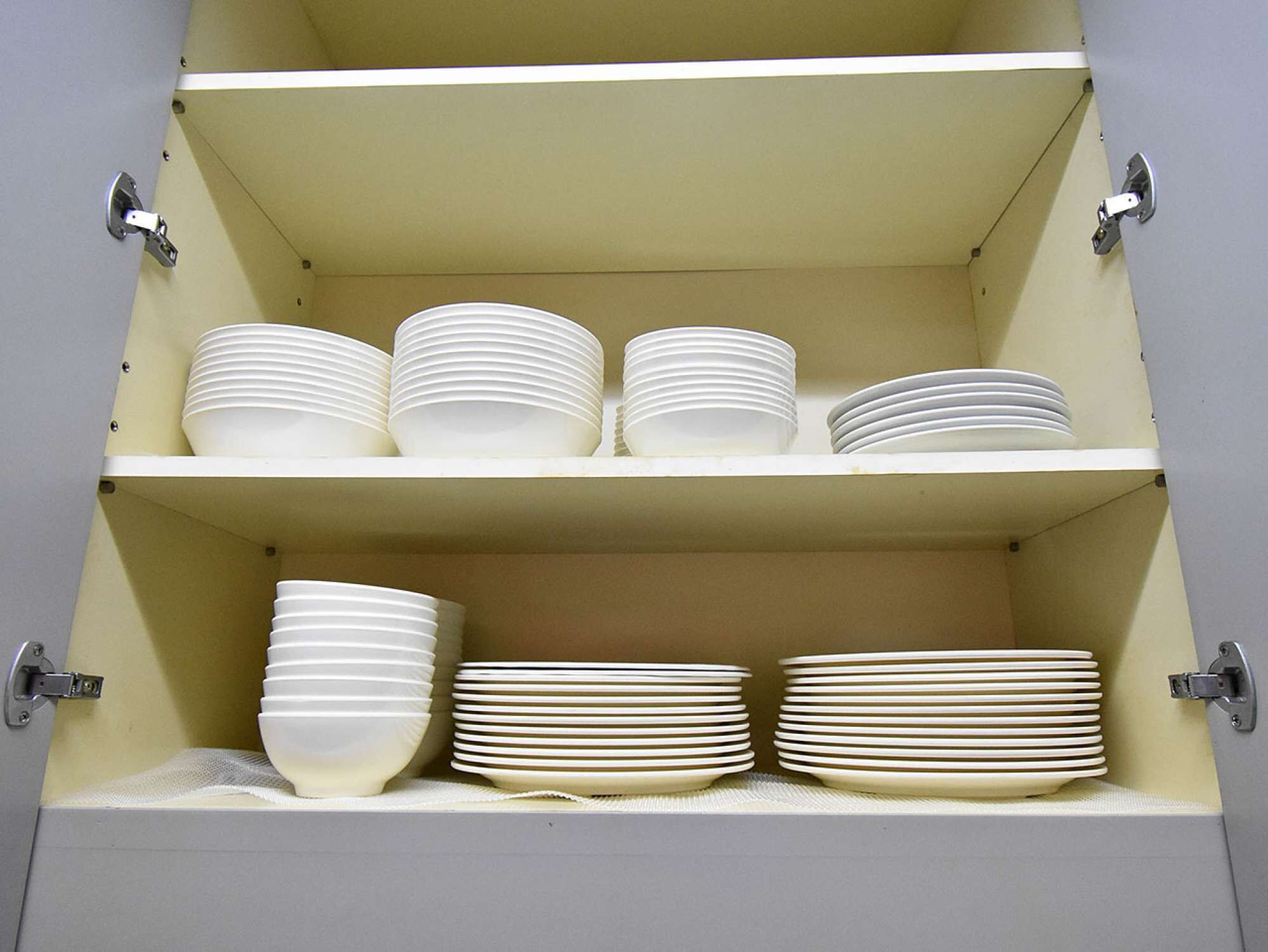 Un mueble con tres repisas, cada una con pilas de platos blancos.