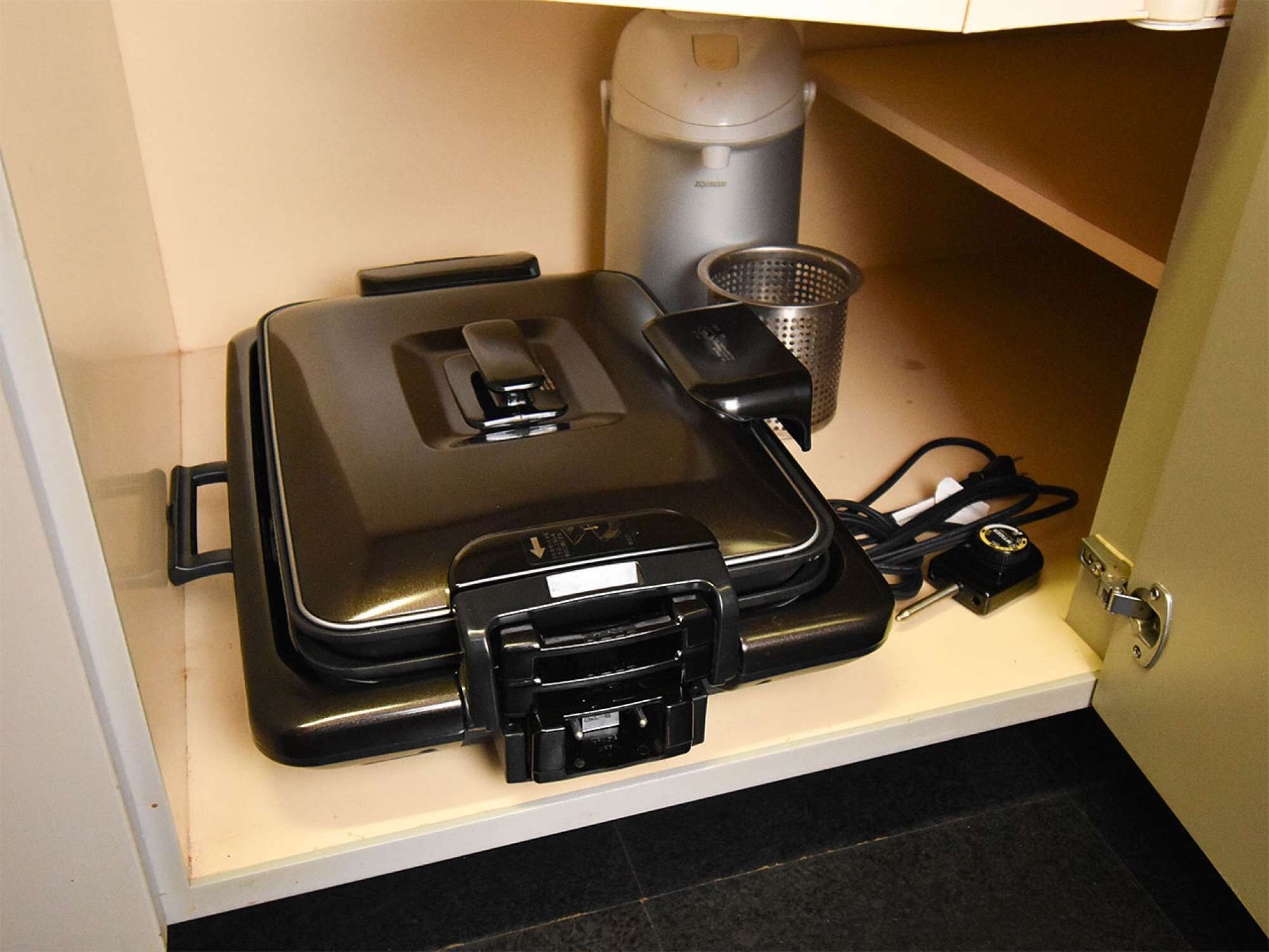 A compact kitchen with a coffee maker, a kettle, and a portable iron on a countertop.