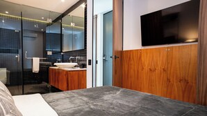 Un dormitorio moderno con una cama grande, un armario de madera, televisor montado y un baño con cabina de ducha de vidrio.