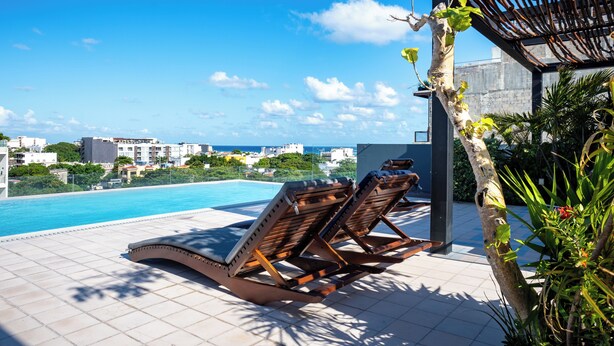 Un área de piscina en la azotea con sillones reclinables y vistas del horizonte de la ciudad.