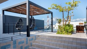 Un espacio exterior moderno con una zona de estar cubierta, escalones que conducen a una terraza y una vista de una torre de comunicaciones alta al fondo.
