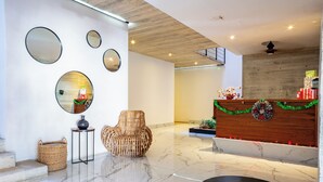 Un vestíbulo moderno con mostrador de recepción, una silla de mimbre y un espejo grande en la pared.