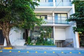Ein modernes, zweistöckiges Gebäude mit einem Balkon, einer Treppe zum Eingang und einem Baum davor.