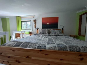 A bedroom with a bed, a desk, a window, and a painting on the wall.