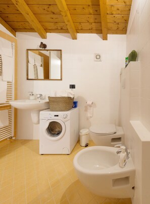 Casa de banho compacta com máquina de lavar roupa, lavatório, sanita e bidé.