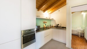 Une cuisine de taille réduite avec des meubles blancs, des appareils en acier inoxydable et un plafond en bois.