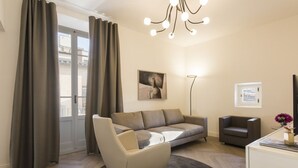 En moderne stue med sofa, stol, skrivebord, gulvlampe og et maleri på væggen.