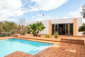 Uma casa moderna com piscina, varanda coberta e um pássaro no telhado.