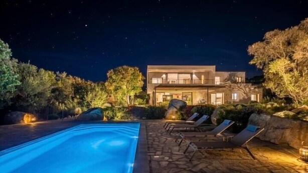 Una casa moderna con piscina, patio de piedra y sillones de descanso.
