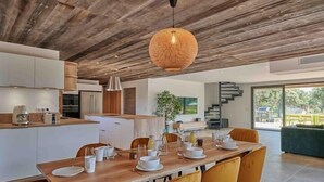 Una cocina moderna con armarios blancos, una mesa de comedor de madera para cuatro personas y una lámpara colgante grande.