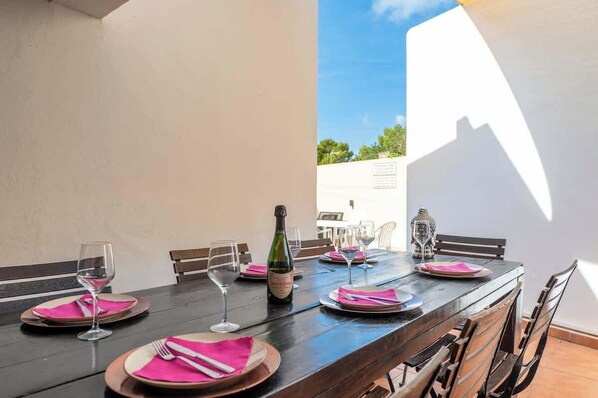 A dining table set for six with pink napkins, wine glasses, and a bottle of champagne.