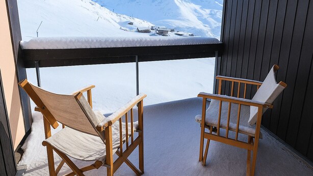 Ein Balkon mit zwei Holzstühlen, Blick auf einen schneebedeckten Berg und klarem Himmel.