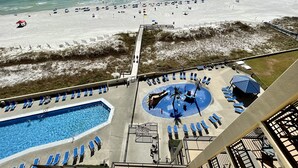 Uitzicht op het strand vanaf een hotelbalkon met een zwembad en ligbedden.