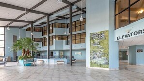 Een ruime lobby met meerdere verdiepingen, een groot zitgedeelte en een muurschildering van een waterval.
