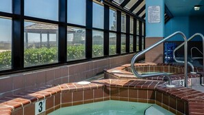 Een hoek met een jacuzzi, betegelde muren en grote ramen.