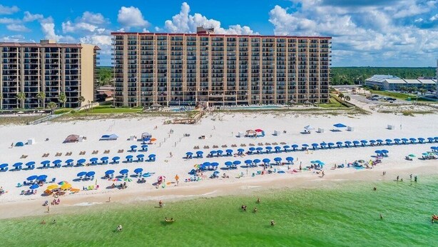 Hotel aan het strand met meerdere hoge gebouwen, een zandstrand met parasols en een heldere lucht.