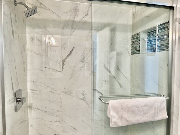 A glass-enclosed shower with a handheld showerhead and a towel rack with a towel.