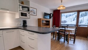 A modern kitchen with white cabinets, a wooden dining table, and chairs. There is a window with a view of a snowy landscape. - Bright 2-Rooms on Slopes, Near Shops, South Balcony (Méribel)