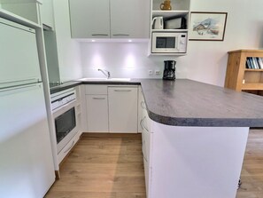 A kitchen with white cabinets, a microwave, a coffee maker, and a wooden floor. - Bright 2-Rooms on Slopes, Near Shops, South Balcony (Méribel)