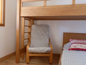 A bunk bed with a wooden ladder, a single bed with patterned bedding, and a chair with a patterned cushion. - Bright 2-Rooms on Slopes, Near Shops, South Balcony (Méribel)