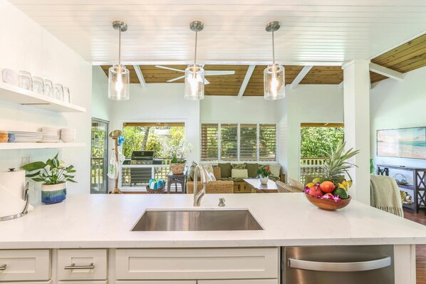 A modern kitchen with a large island, stainless steel appliances, pendant lighting, and a view to an outdoor patio area.