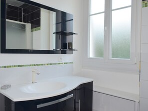 Een badkamer met een wit wastafel, een spiegel en een raam.