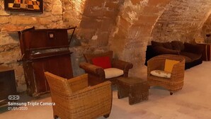 Une pièce chaleureuse et rustique, avec des murs en pierre et une cheminée. On y trouve des meubles en osier, dont un canapé et des fauteuils, ainsi qu'une petite table en bois.