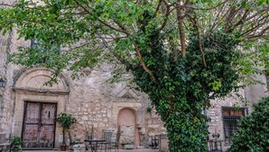 Une cour extérieure avec des murs en pierre, un arbre et une table entourée de chaises.