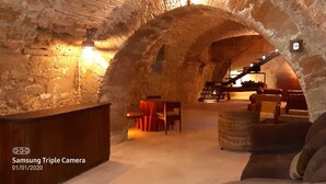 Une pièce souterraine dotée d’une arche en pierre, d’un comptoir en bois, d’un canapé et d’un escalier menant à un autre niveau.