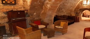 Une pièce chaleureuse et rustique, avec des murs en pierre et une cheminée. On y trouve des meubles en osier, dont un canapé et des fauteuils, ainsi qu'une petite table en bois.
