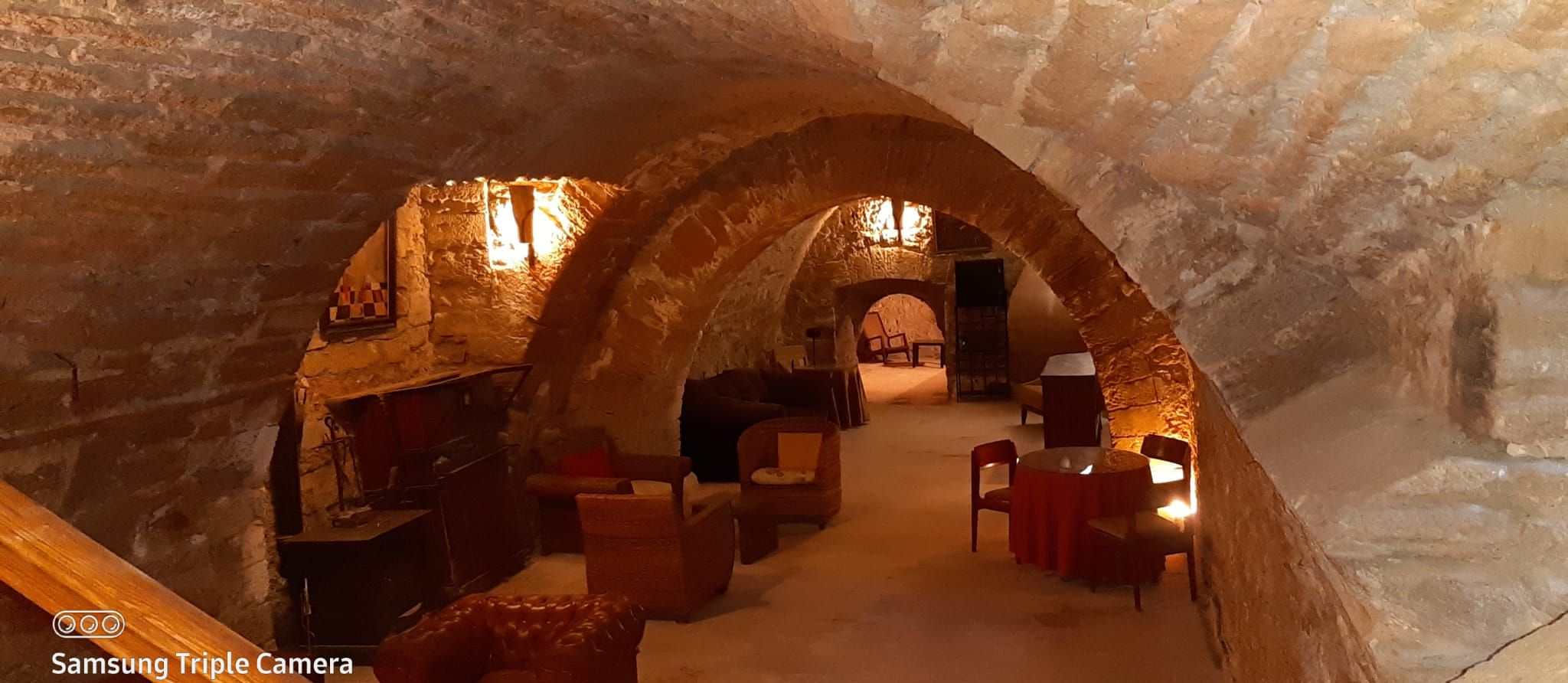 Un intérieur aux murs de pierre, avec un coin salon confortable, une cheminée et une table en bois.
