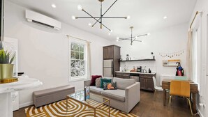 Un soggiorno moderno con un divano, un tavolino da caffè e un tappeto decorato. Si intravede sullo sfondo una zona cucina con frigorifero e tavolo da pranzo.