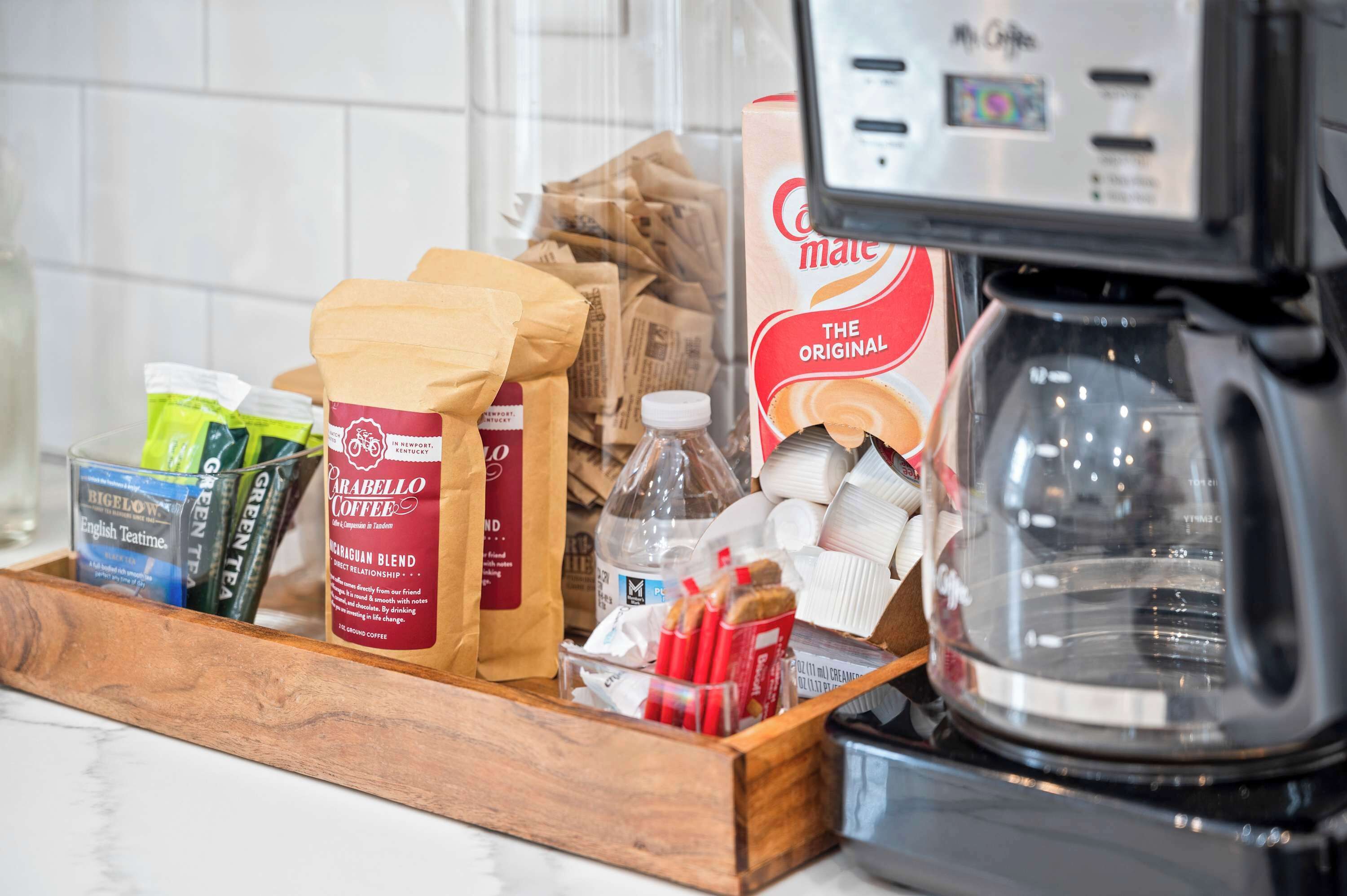 A coffee maker and a tray with coffee packets, a bottle, and paper bags.