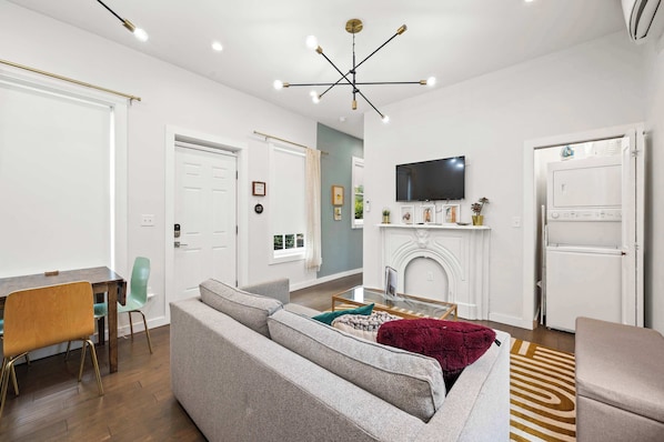 Una sala de estar moderna con un sofá gris, una mesa de comedor con sillas, un televisor montado en la pared y una chimenea.