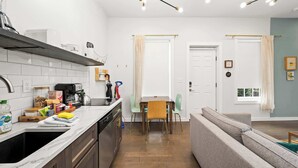 Una cucina moderna con lavastoviglie, forno a microonde e macchina da caffè. C'è un tavolo da pranzo con sedie e un divano nella zona living.