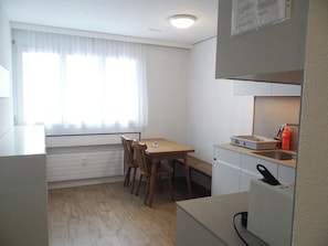 A compact kitchen with a dining area, a window with curtains, and a built-in oven.