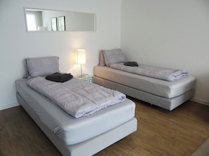 Two single beds with patterned bedding, a bedside lamp, and a mirror on the wall.