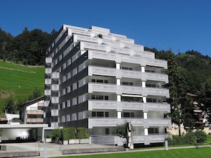 A multi-story building with balconies, a parking area, and a sculpture in the foreground.