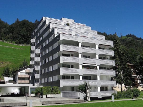 A multi-story building with balconies, a parking area, and a sculpture in the foreground.