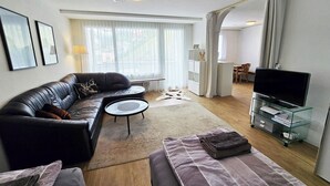 A modern living room with a black leather sofa, a glass TV stand, and a dining area in the background. - Sunnmatt 752 Appartement/Fewo 3-Bettwohnung by Interhome (Engelberg)