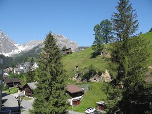 A mountain village with traditional wooden houses, a clear sky, and snow-capped mountains in the background.