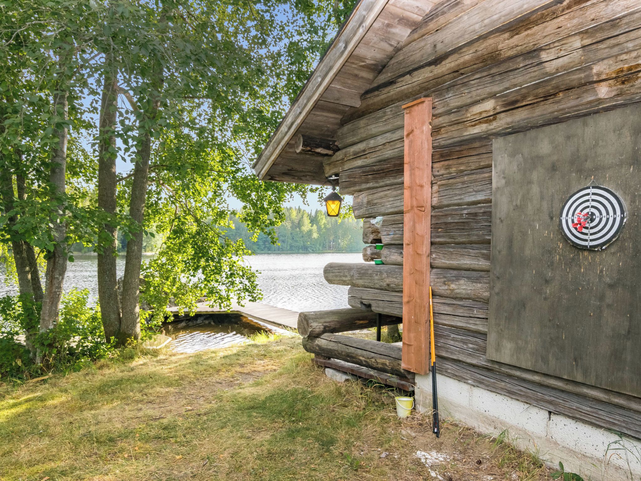Maalaishenkinen mökki, jossa on puinen ulkoverhous, pieni kuisti ja seinässä maalitaulu.