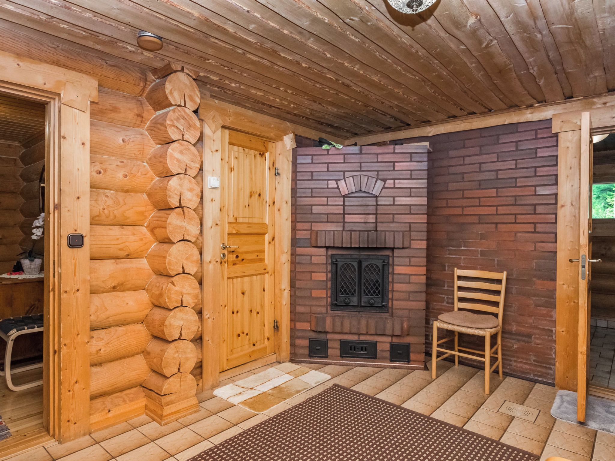 A log cabin interior with a wooden door, a brick fireplace, and a chair.