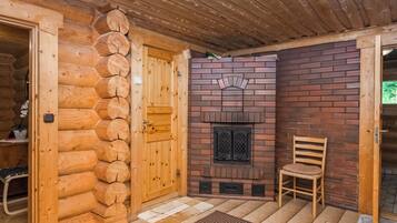 A log cabin interior with a wooden door, a brick fireplace, and a chair.