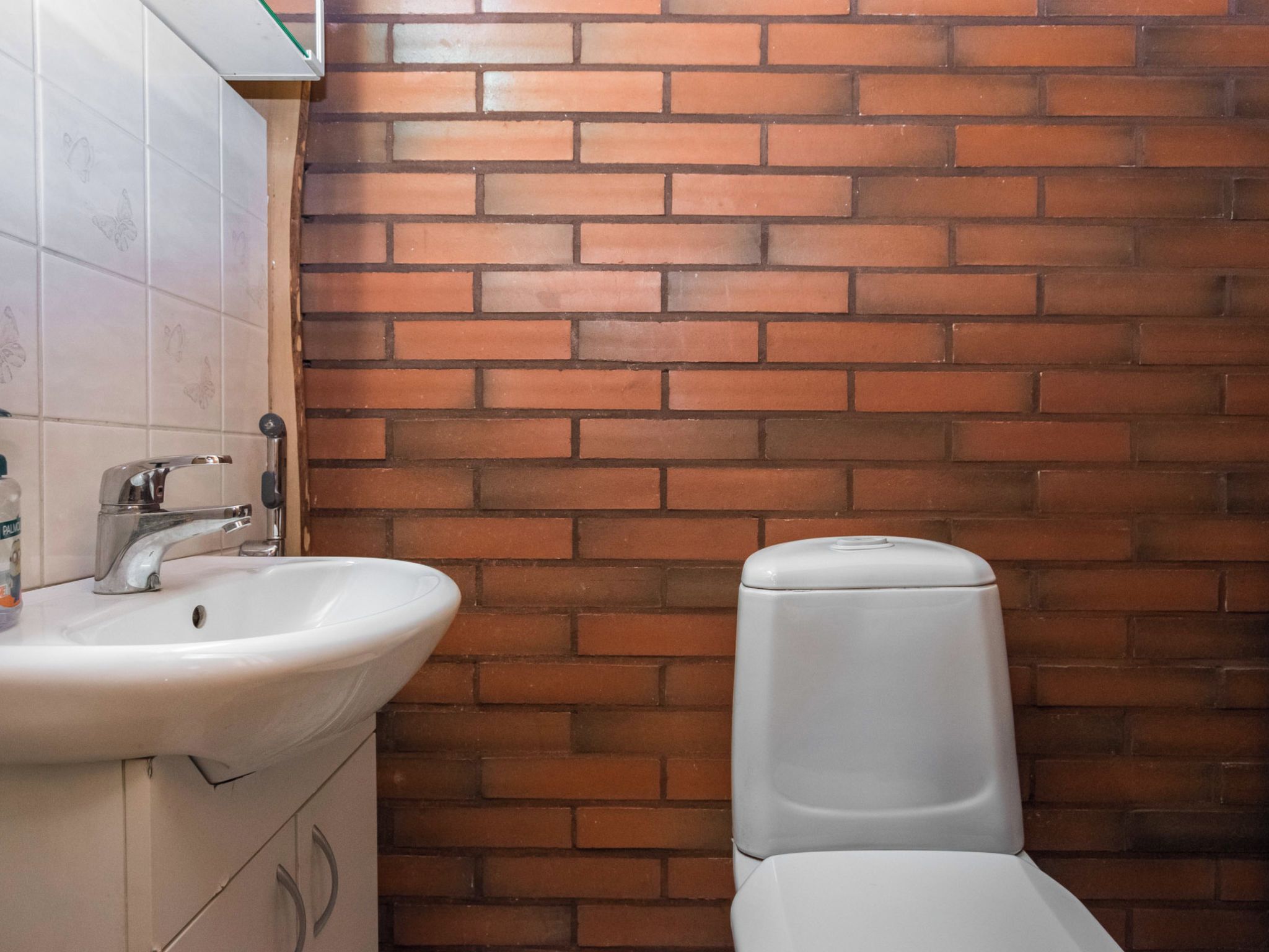 A bathroom with a white sink, a toilet, and a tiled wall with a brick pattern.
