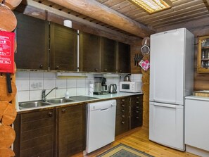 A kitchen with wooden cabinets, a sink, a dishwasher, a microwave, and a refrigerator. - Rasilinna by Interhome (Mikkeli)